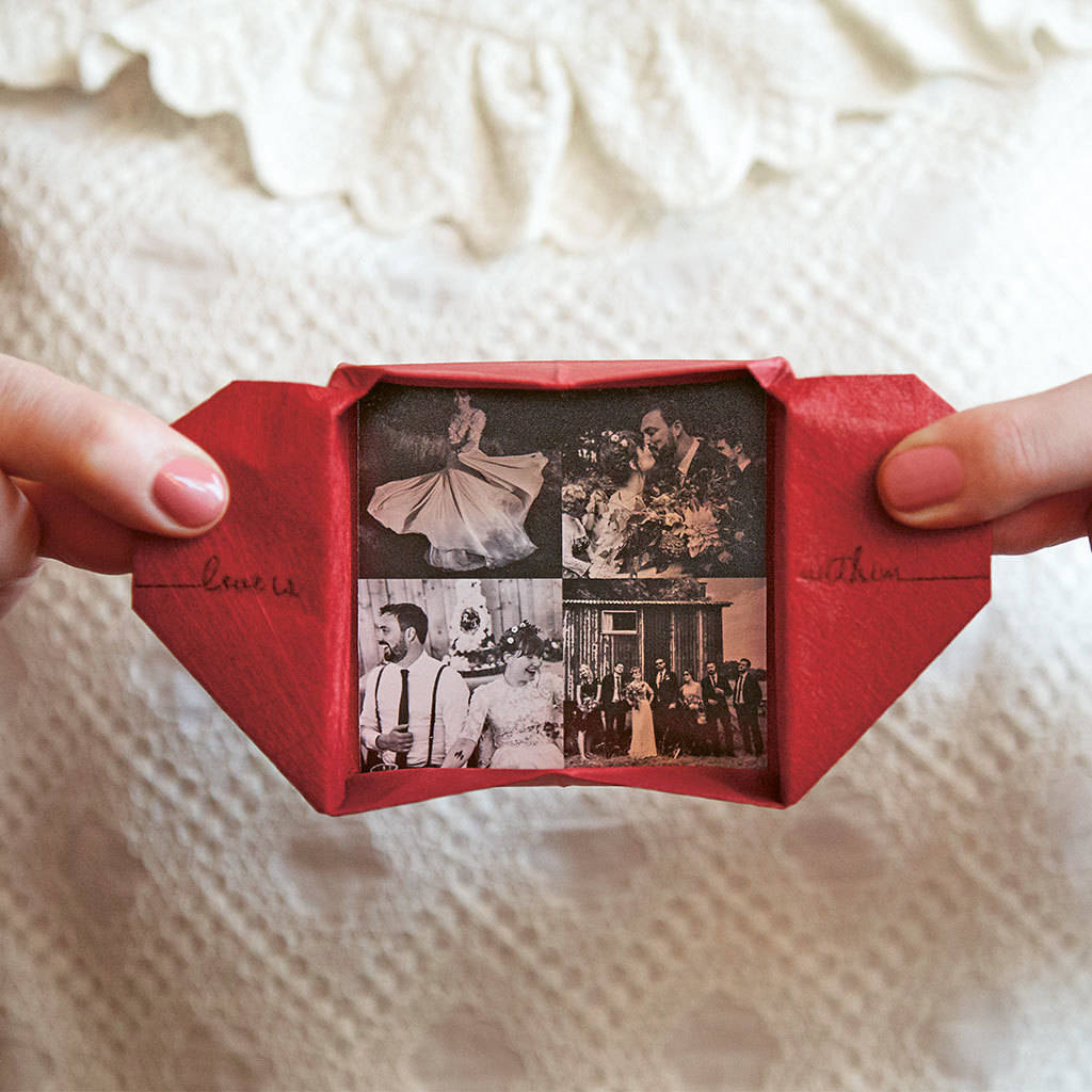 A hand holding an origami heart keepsake with a photographic insert showing various images of a couple, demonstrating the keepsake's mechanism and design. Personalised origami heart keepsake handmade UK paper anniversary gift